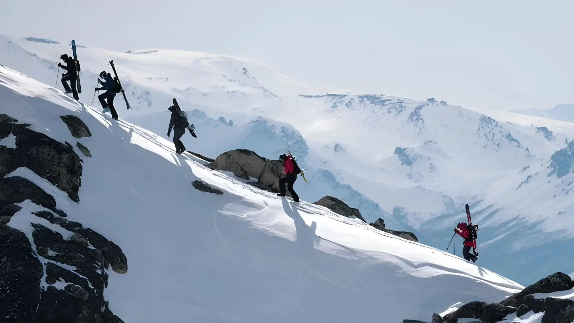 back country hikers with skis and snowboard up the side of a mountain